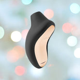 The LELO SONA Cruise Sonic Wave Clitoral Massager in black and gold, with its sleek, matte finish, stands out against a blurred, colorful bokeh background. This cutting-edge device combines Sonic Pulse technology and customizable pleasure settings with a modern ergonomic design and waterproof capabilities for an unparalleled experience.